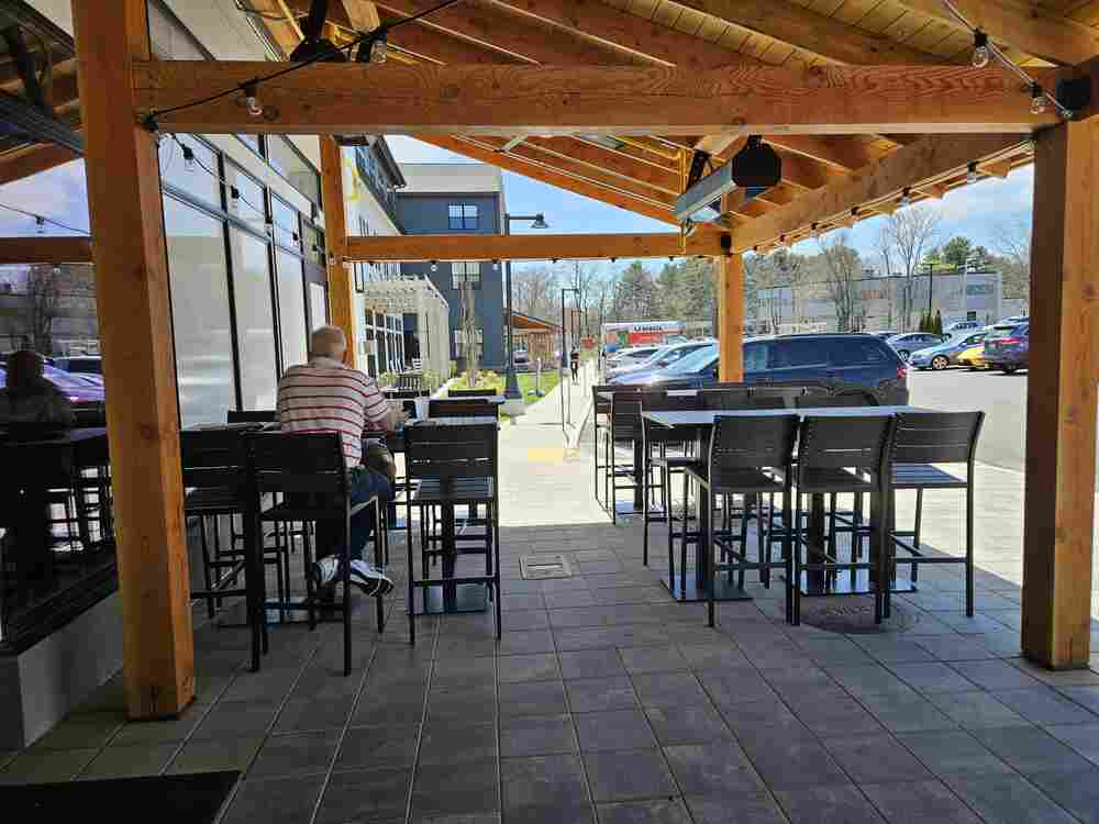 Photo of a person sitting at a table, also multiple other tables on the outdoor patio